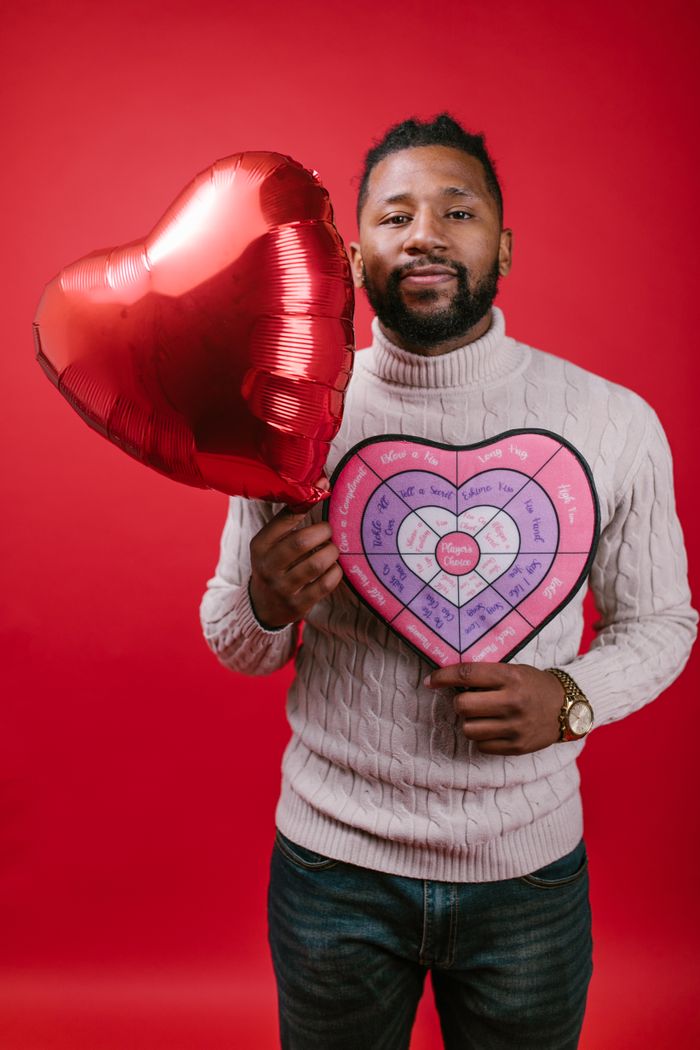 A man holding a heart-shaped balloon and a Valentine's gift against a red backdrop.